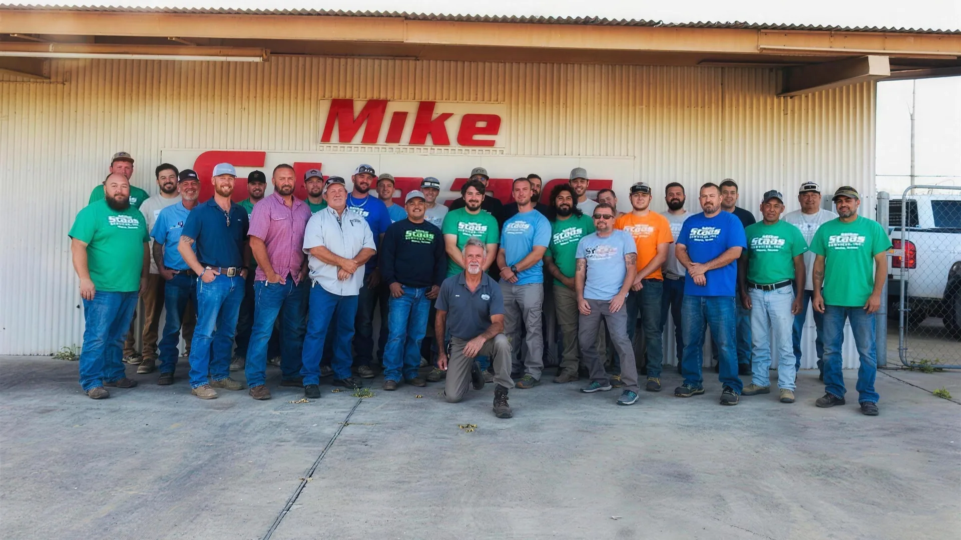 The Mike Staas Services crew in green and blue shirts, standing in front of the company building in Waco